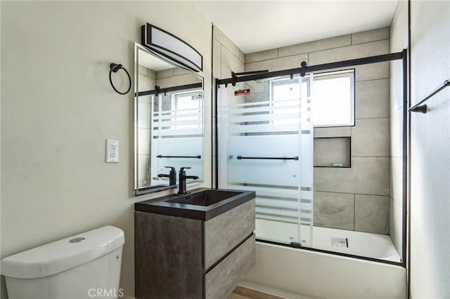 bathroom featuring toilet, shower / bath combination with glass door, and vanity