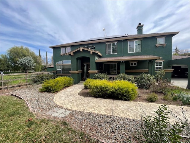 view of front of home with solar panels, fence, a chimney, and stucco siding