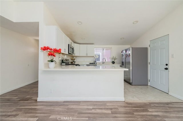 kitchen featuring light wood finished floors, a peninsula, stainless steel appliances, light countertops, and white cabinetry