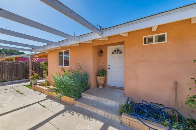 entrance to property featuring a patio, fence, and stucco siding