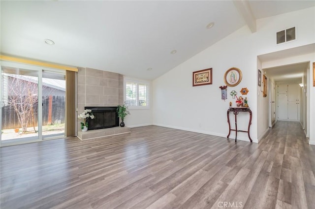 unfurnished living room with baseboards, visible vents, a tiled fireplace, wood finished floors, and vaulted ceiling with beams