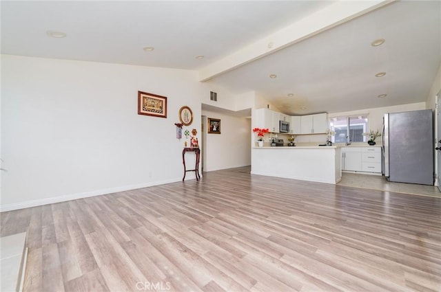 unfurnished living room with lofted ceiling with beams, light wood-style floors, visible vents, and baseboards