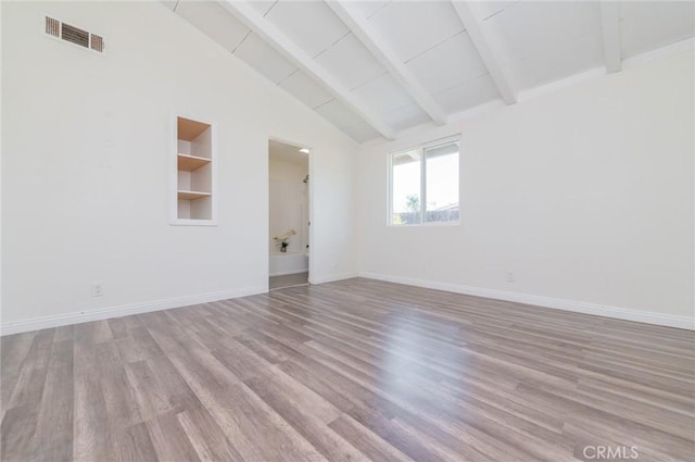 spare room with visible vents, beamed ceiling, baseboards, and wood finished floors