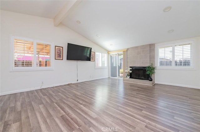 unfurnished living room featuring baseboards, a tiled fireplace, lofted ceiling with beams, and light wood finished floors