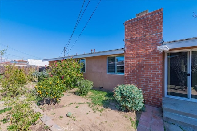 view of side of property with crawl space, a chimney, and stucco siding