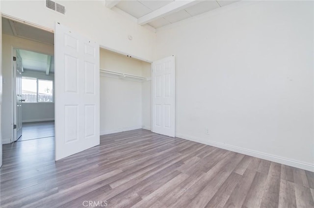 unfurnished bedroom with beamed ceiling, wood finished floors, visible vents, and baseboards