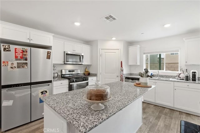 kitchen with stainless steel appliances, visible vents, white cabinets, a sink, and light wood-type flooring