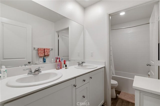 full bath with toilet, double vanity, a sink, and wood finished floors