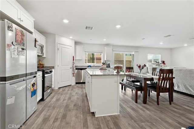 kitchen featuring visible vents, white cabinets, light wood-style flooring, a kitchen island, and stainless steel appliances