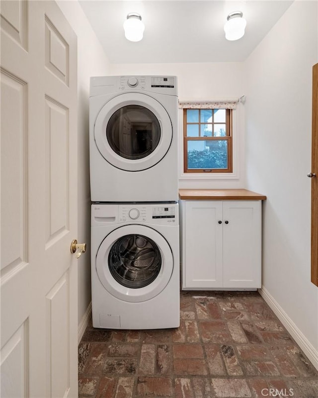 washroom with brick floor, baseboards, cabinet space, and stacked washing maching and dryer