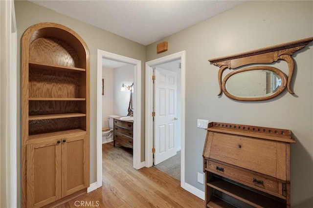 hall with light wood-style flooring, baseboards, and a sink