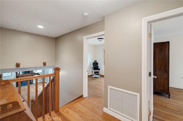 hall with an upstairs landing, baseboards, visible vents, and light wood finished floors