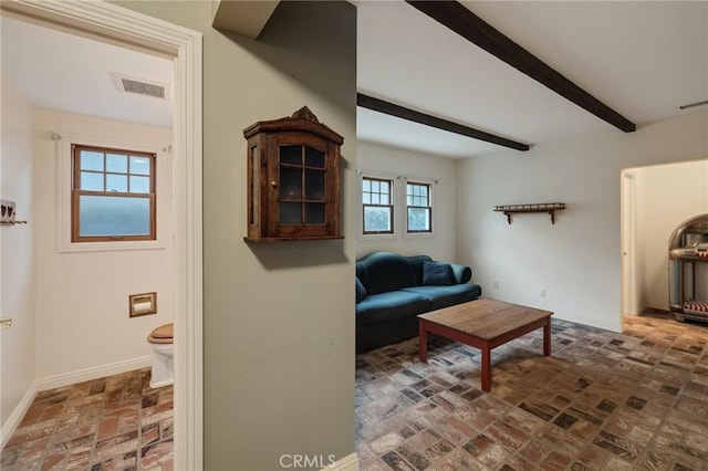 living area featuring brick floor, beam ceiling, visible vents, and baseboards