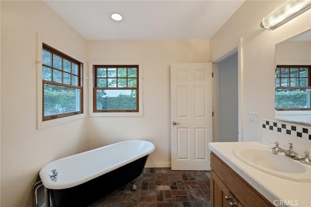 bathroom featuring a freestanding bath, tasteful backsplash, brick floor, and vanity