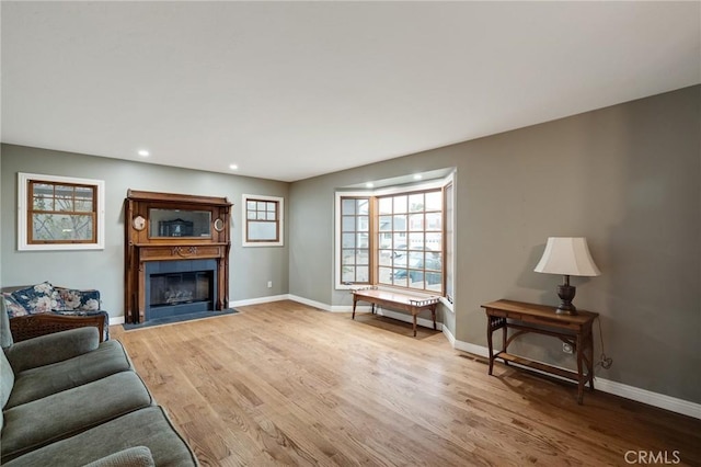 living room with a fireplace with flush hearth, light wood-type flooring, baseboards, and recessed lighting