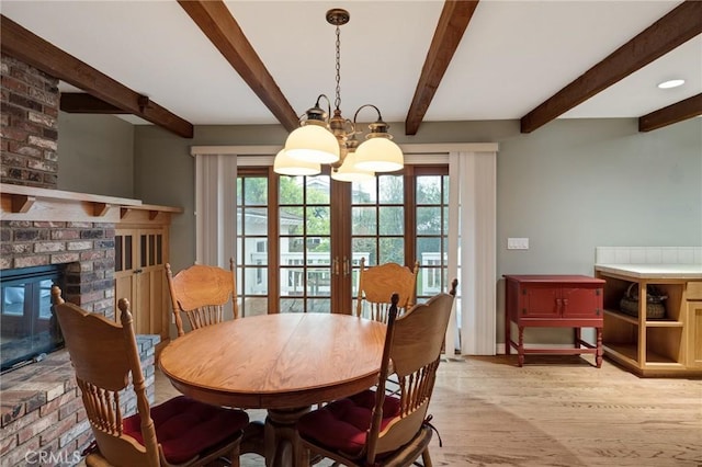 dining area featuring light wood-style floors, a brick fireplace, a healthy amount of sunlight, and an inviting chandelier