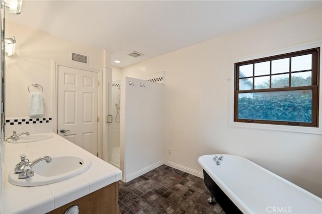 bathroom with visible vents, a freestanding bath, a stall shower, a sink, and baseboards