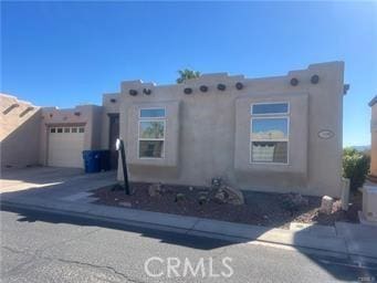 pueblo revival-style home featuring a garage, driveway, and stucco siding