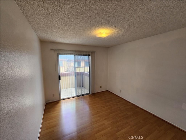 empty room with a textured ceiling, wood finished floors, and a textured wall