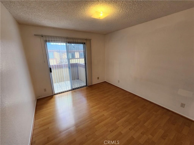 empty room featuring a textured ceiling, baseboards, and wood finished floors