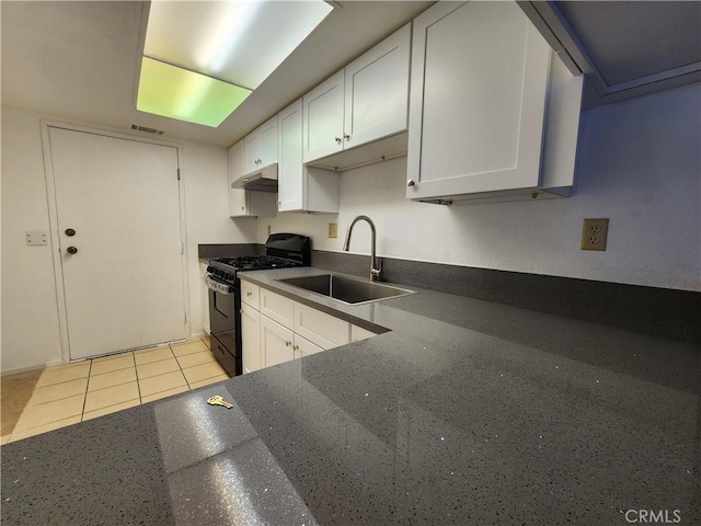 kitchen with light tile patterned floors, black gas stove, under cabinet range hood, white cabinetry, and a sink