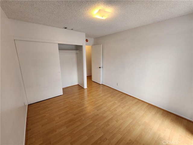 unfurnished bedroom featuring a textured ceiling, a closet, wood finished floors, and visible vents