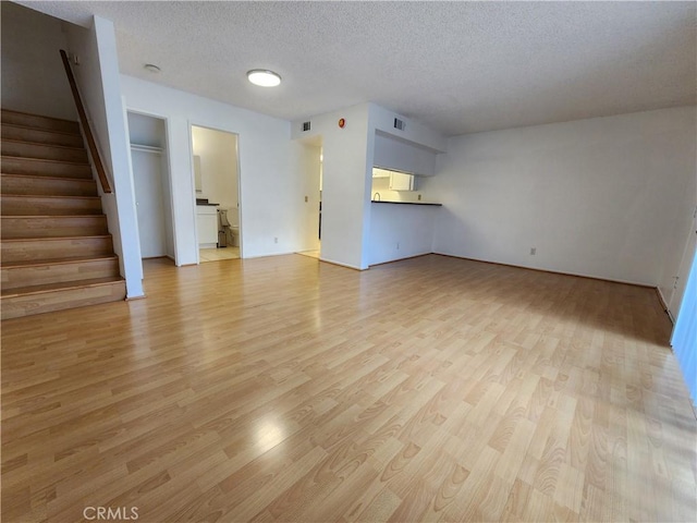 unfurnished living room featuring light wood-style flooring, stairs, visible vents, and a textured ceiling