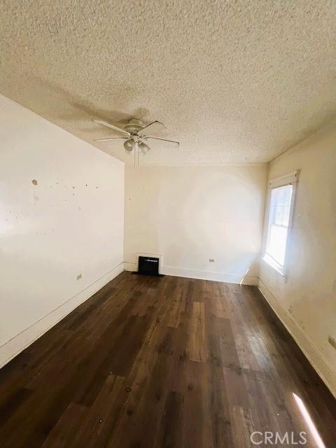 empty room featuring baseboards, a textured ceiling, ceiling fan, and dark wood-style flooring