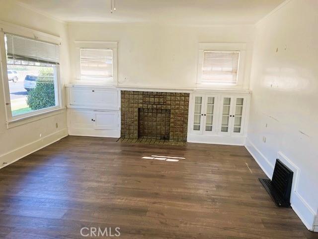 unfurnished living room featuring visible vents, dark wood finished floors, a tiled fireplace, and ornamental molding