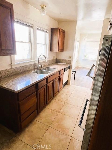 kitchen with light tile patterned flooring, brown cabinetry, white dishwasher, and a sink