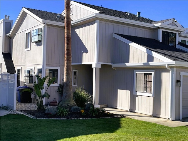 rear view of property featuring a garage, a shingled roof, and a lawn