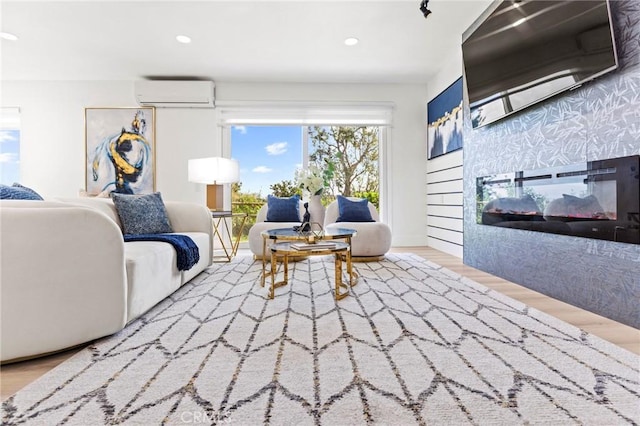 living area featuring a glass covered fireplace, a wall unit AC, recessed lighting, and wood finished floors