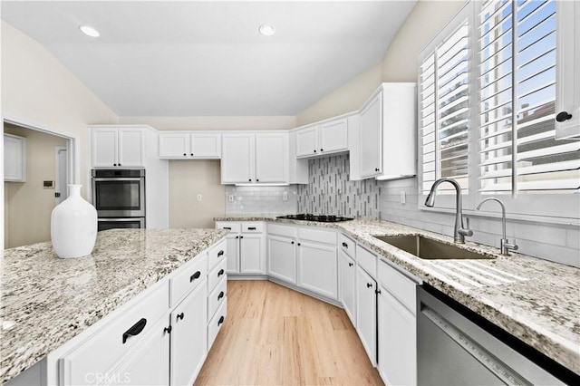 kitchen featuring light wood finished floors, decorative backsplash, appliances with stainless steel finishes, vaulted ceiling, and a sink