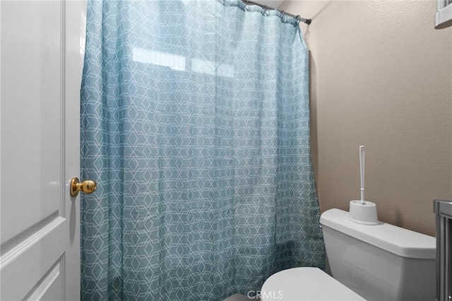 full bath featuring a shower with curtain, a textured wall, and toilet