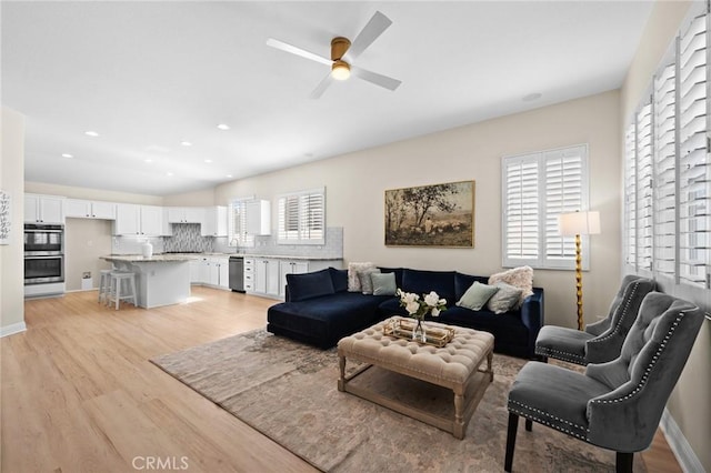 living area featuring light wood-style flooring, baseboards, ceiling fan, and recessed lighting