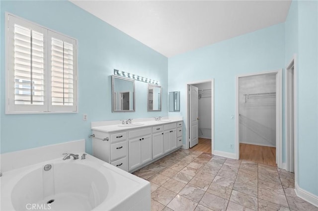 bathroom featuring a garden tub, a spacious closet, double vanity, and a sink