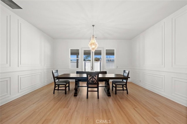 dining room featuring a notable chandelier, light wood-type flooring, and a decorative wall