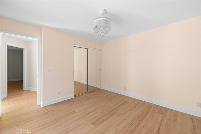 unfurnished bedroom with baseboards, a closet, a chandelier, and light wood-style floors