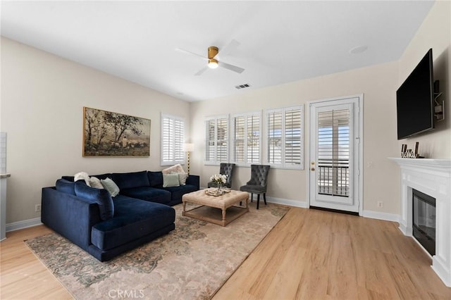 living room with a ceiling fan, a glass covered fireplace, visible vents, and light wood-style flooring