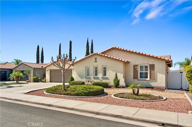 mediterranean / spanish-style home featuring stucco siding, concrete driveway, a gate, a garage, and a tiled roof