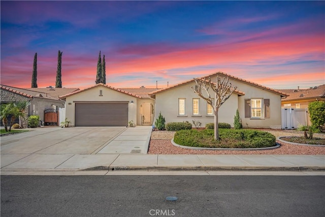 mediterranean / spanish house featuring stucco siding, concrete driveway, a gate, fence, and a garage