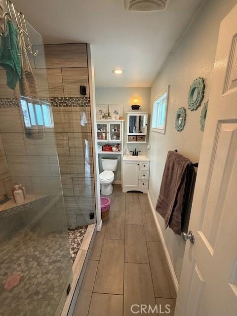 bathroom featuring visible vents, toilet, wood tiled floor, vanity, and a shower stall