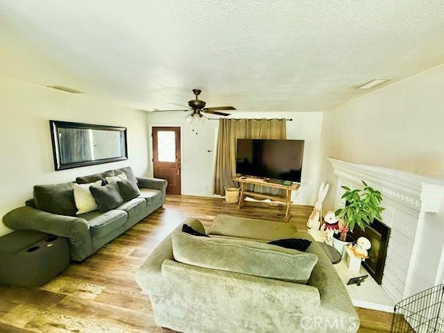 living area featuring ceiling fan, a fireplace, a textured ceiling, and wood finished floors