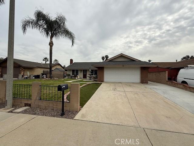 ranch-style home featuring an attached garage, fence, concrete driveway, and a front yard