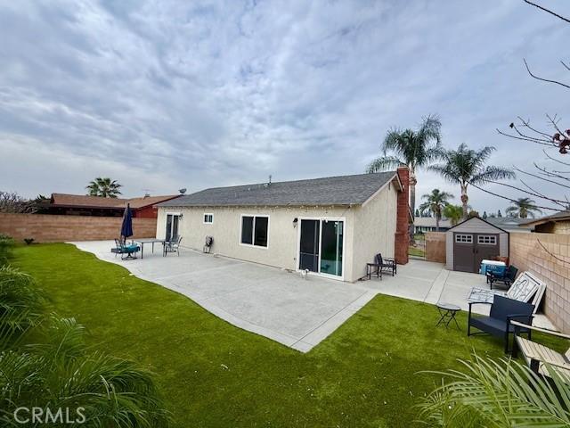 rear view of property featuring an outbuilding, stucco siding, a storage shed, a patio area, and a fenced backyard