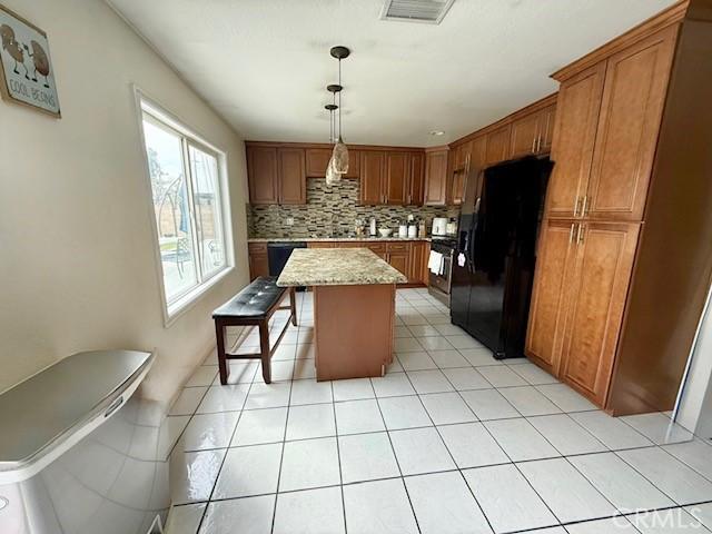 kitchen featuring tasteful backsplash, visible vents, brown cabinetry, a kitchen island, and black appliances