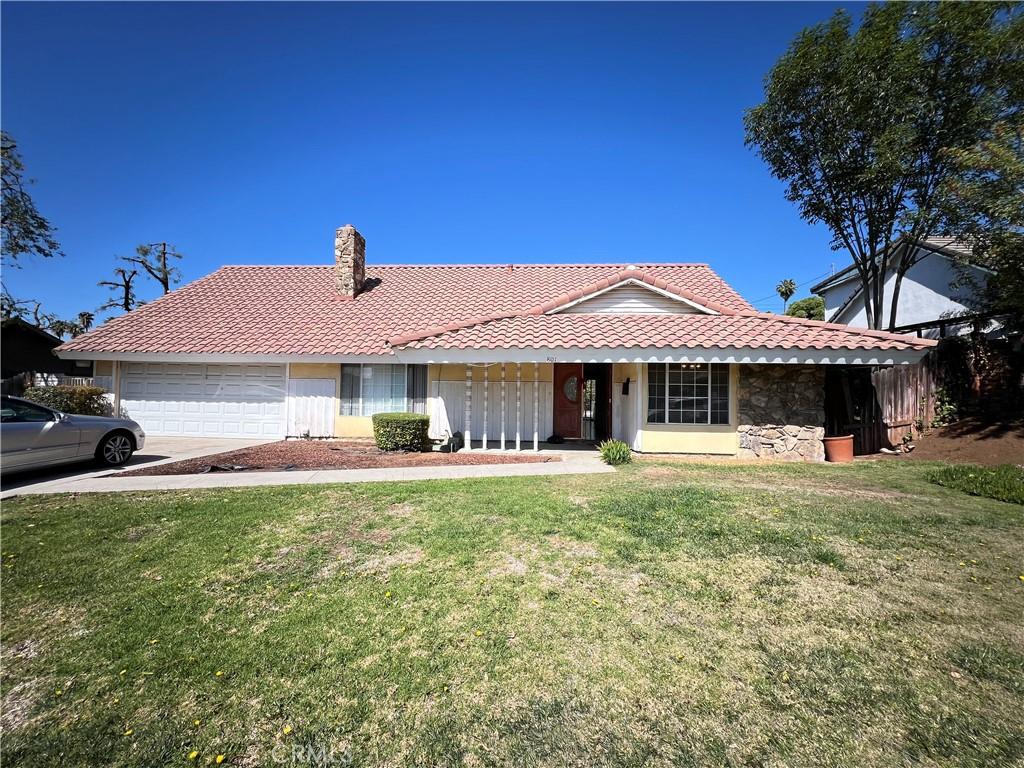 ranch-style house featuring a tiled roof, a front lawn, and a chimney