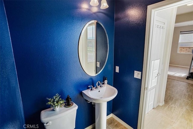 half bath with toilet, baseboards, a sink, and a textured wall