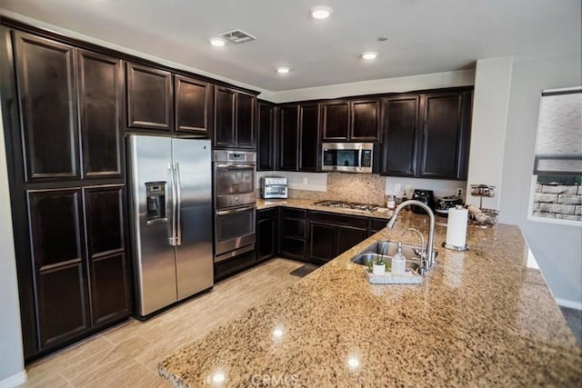 kitchen with appliances with stainless steel finishes, a sink, visible vents, and light stone countertops