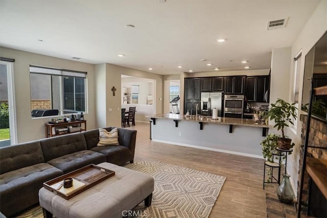 living area with baseboards, light wood-type flooring, visible vents, and recessed lighting